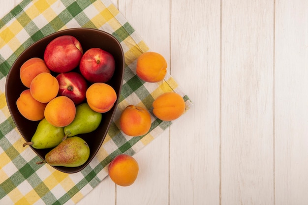 Vue de dessus des fruits comme poire pêche abricot dans un bol sur un tissu à carreaux et sur fond de bois avec espace copie