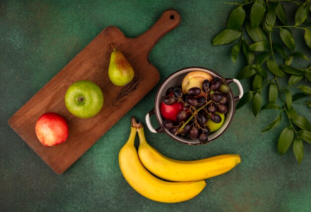 Vue de dessus des fruits comme poire pêche raisin en pot et sur une planche à découper avec des feuilles sur fond vert