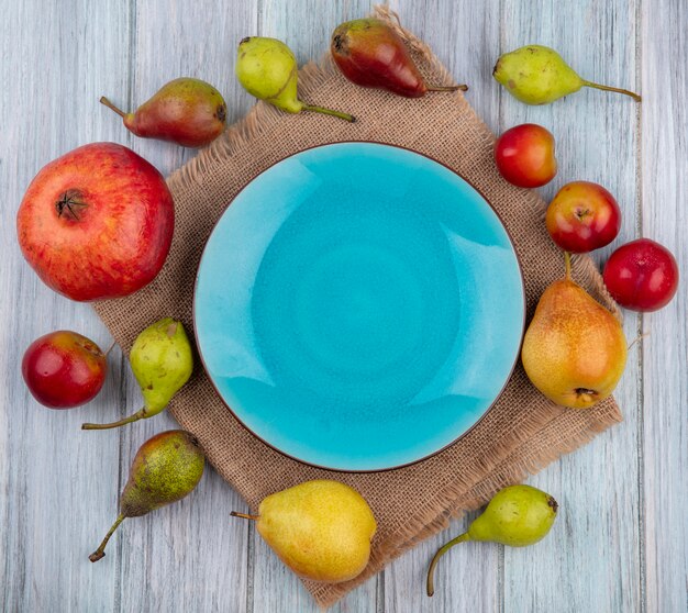 Photo gratuite vue de dessus des fruits comme prune pêche grenade autour d'une assiette vide sur un sac sur une surface en bois