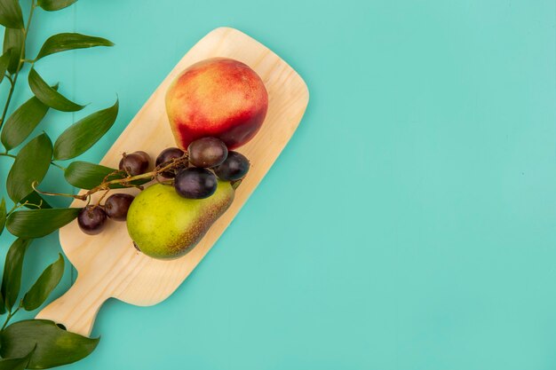 Vue de dessus des fruits comme raisin poire pêche sur planche à découper avec des feuilles sur fond bleu avec espace copie