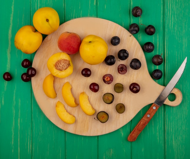 Vue de dessus des fruits dans leur ensemble à moitié abricots et baies de prunelle avec un couteau sur une planche à découper et sur fond vert