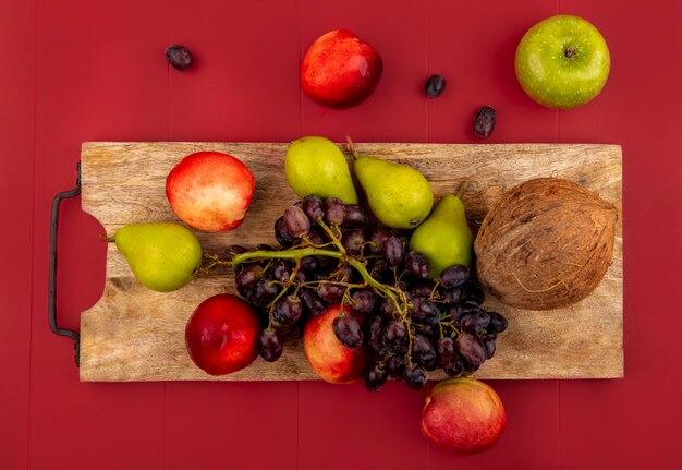 Photo gratuite vue de dessus des fruits d'été frais tels que la poire de raisin coco sur une planche de cuisine en bois sur fond rouge