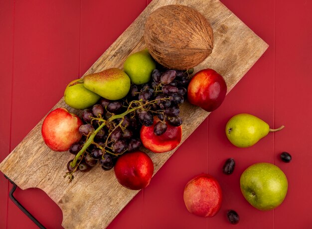 Vue de dessus des fruits frais tels que peargrapepeach sur une planche de cuisine en bois sur fond rouge