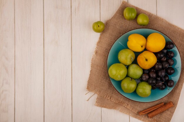 Vue De Dessus De Fruits Frais Tels Que Les Prunes De Cerises Vertes Sur Un Plat Bleu Sur Un Tissu De Sac Sur Un Fond En Bois Blanc Avec Espace De Copie