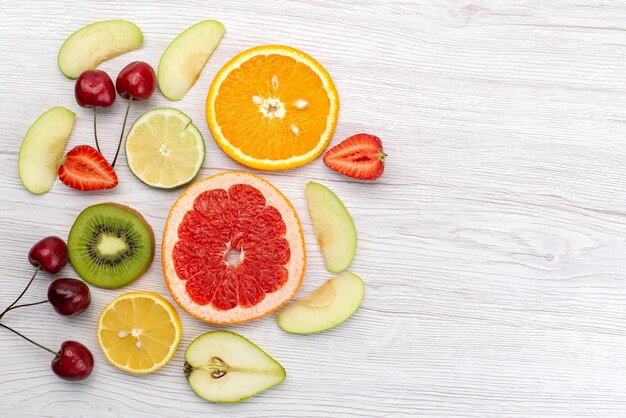 Une vue de dessus des fruits frais tranchés moelleux et mûrs sur un bureau blanc, couleur de vitamine fraîche de fruits