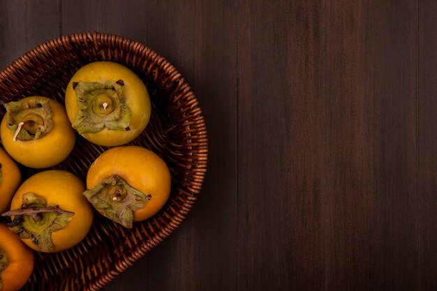 Vue de dessus des fruits de kaki non mûrs sur un seau sur une table en bois avec espace copie