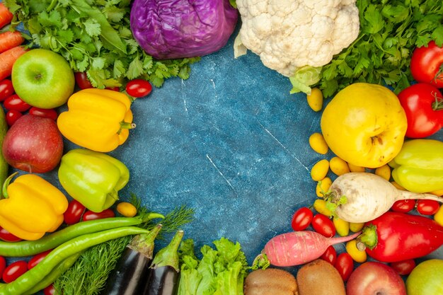 Vue de dessus fruits et légumes tomates cerises cumcuat coing pommes aubergines radis coriandre chou rouge chou-fleur sur table bleue