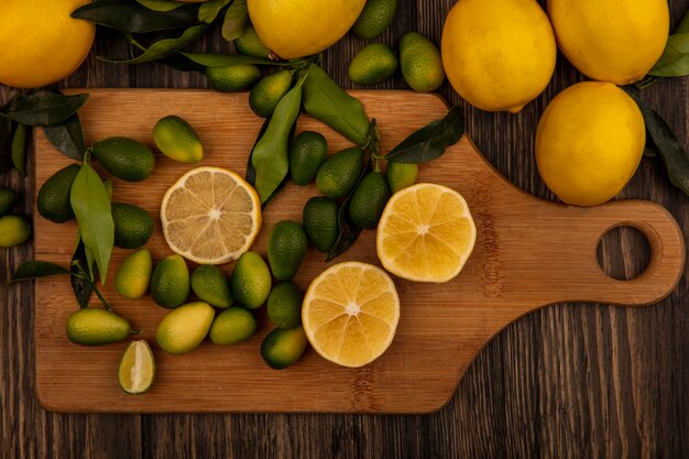 Vue de dessus de fruits riches en vitamines tels que les citrons et les kinkans sur une planche de cuisine en bois sur une surface en bois