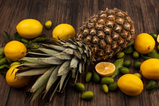 Vue de dessus de fruits sains tels que les citrons d'ananas et les kinkans isolés sur un fond en bois