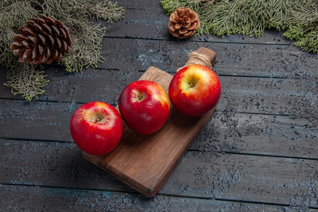 Vue de dessus des fruits sur la table trois pommes sur une planche à découper en bois entre les branches avec des cônes