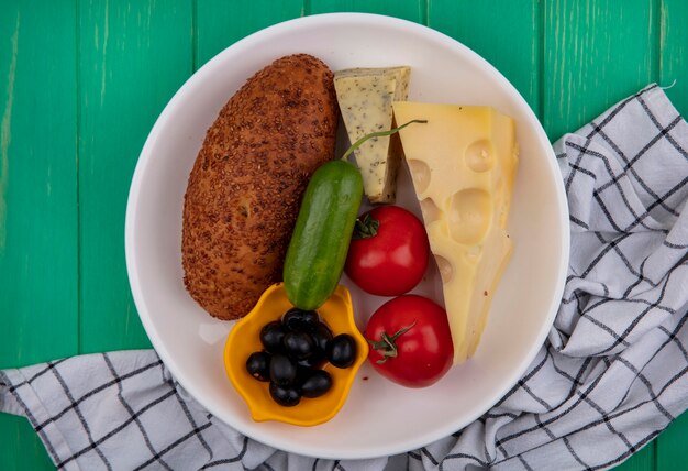 Vue de dessus de la galette de sésame sur une plaque blanche avec du fromage de légumes frais et olives sur un tissu vérifié sur un fond en bois vert