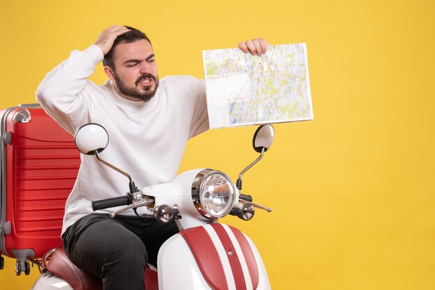 Vue de dessus d'un gars confus assis sur une moto avec une valise dessus tenant une carte sur fond jaune isolé