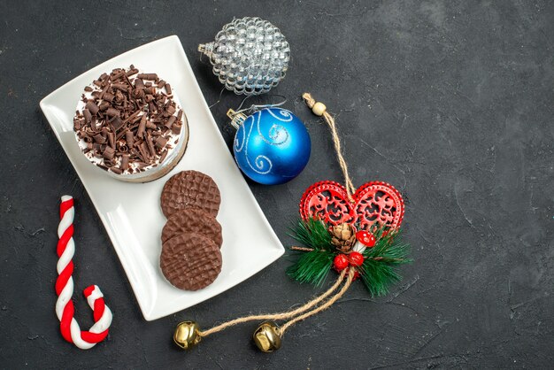 Photo gratuite vue de dessus gâteau au chocolat et biscuits sur plaque rectangulaire blanche jouets d'arbre de noël sur fond sombre isolé