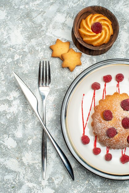 Vue de dessus gâteau aux baies sur plaque ovale blanche biscuits croisés fourchette et couteau à dîner sur surface grise