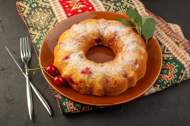 Une vue de dessus gâteau aux cerises rond formé à l'intérieur de la plaque brune sur le bureau sombre gâteau biscuit sucre sucré