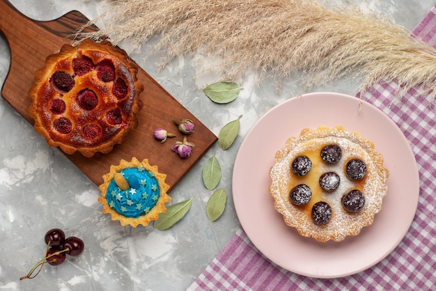 Vue de dessus gâteau aux framboises avec petit gâteau sur la tarte au gâteau de table lumineuse douce aux fruits cerise