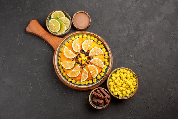 Photo gratuite vue de dessus gâteau à bord bonbons crème au chocolat et limes tranchées dans des bols et gâteau à l'orange sur la planche à découper sur la table