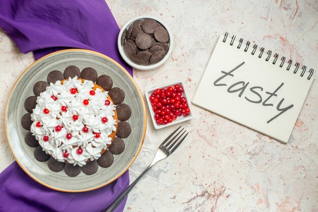 Vue de dessus gâteau avec crème pâtissière et chocolat sur assiette bols châle violet avec fourchette au chocolat et baies savoureuses écrites sur ordinateur portable