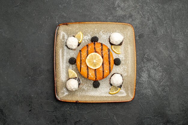 Vue de dessus gâteau délicieux dessert avec des tranches de citron et des bonbons à la noix de coco sur une surface sombre dessert thé gâteau sucré tarte bonbons