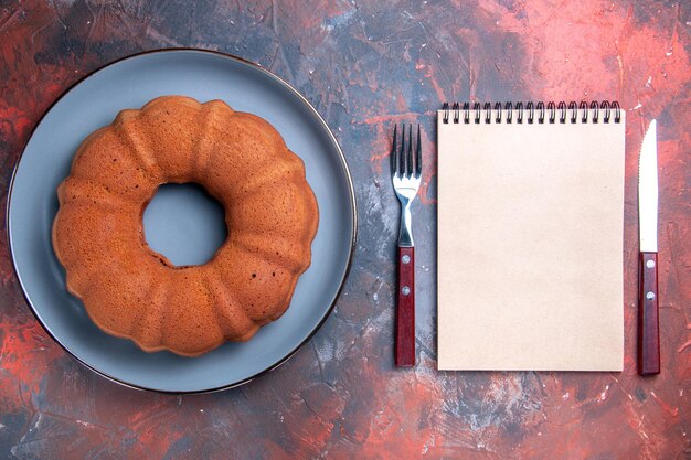 Vue de dessus gâteau fourchette et couteau pour ordinateur portable blanc à côté du gâteau appétissant sur l'assiette