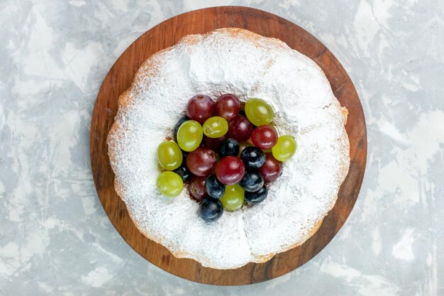 Vue de dessus gâteau en poudre délicieux gâteau cuit au four avec des raisins frais sur un bureau blanc