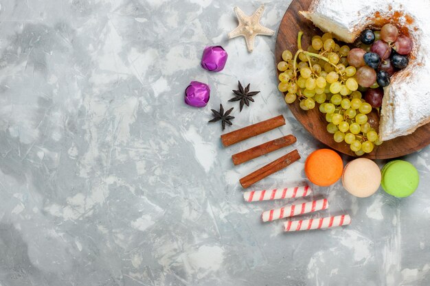 Vue de dessus gâteau en poudre avec raisins cannelle et macarons sur la surface blanche