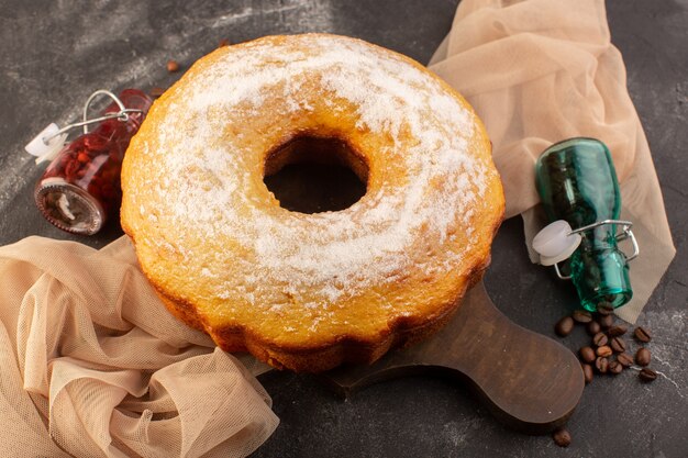 Une vue de dessus gâteau rond cuit avec du sucre en poudre et des graines de café sur le bureau en bois