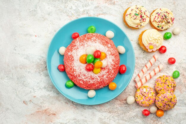 Vue de dessus gâteau rose avec des bonbons colorés sur une surface blanche goodie arc-en-ciel bonbons dessert couleur gâteau