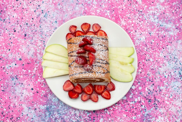 Vue de dessus le gâteau de rouleau avec des fruits à l'intérieur de la plaque blanche sur le fond coloré gâteau biscuit couleur douce