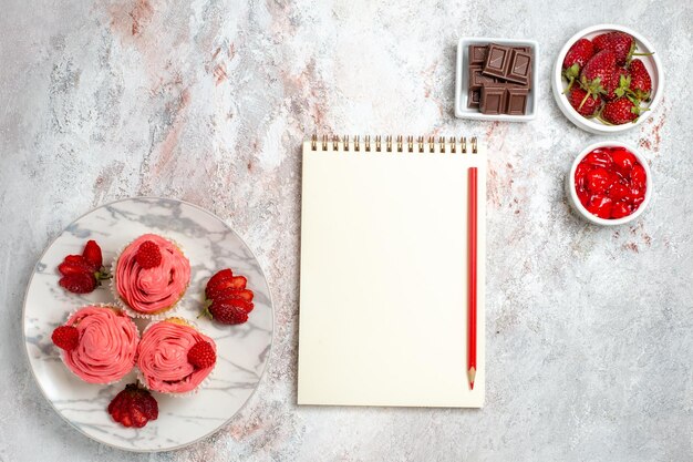 Vue de dessus des gâteaux aux fraises roses avec de la confiture et des barres de chocolat sur une surface blanche