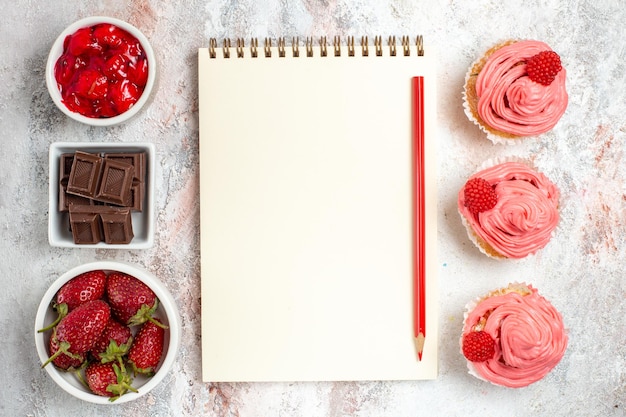 Vue de dessus des gâteaux aux fraises roses avec de la crème sur une surface blanche