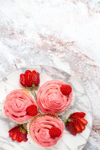 Vue de dessus des gâteaux aux fraises roses avec des fraises rouges fraîches sur une surface blanche