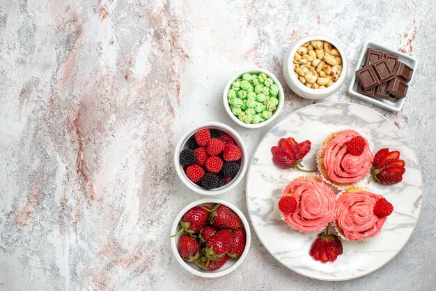 Vue de dessus des gâteaux aux fraises roses avec des noix et des bonbons sur une surface blanche