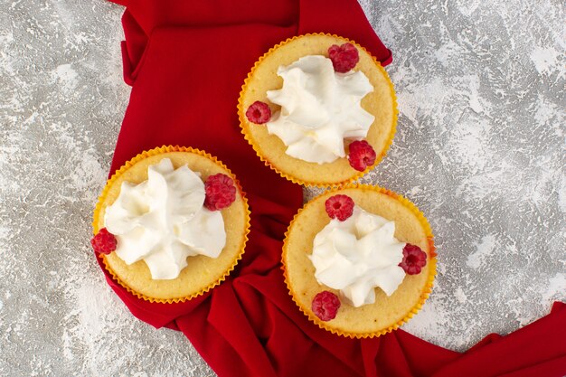 Vue de dessus des gâteaux avec de la crème cuite au four délicieux conçu avec des framboises sur le bureau gris crème sucrée au sucre