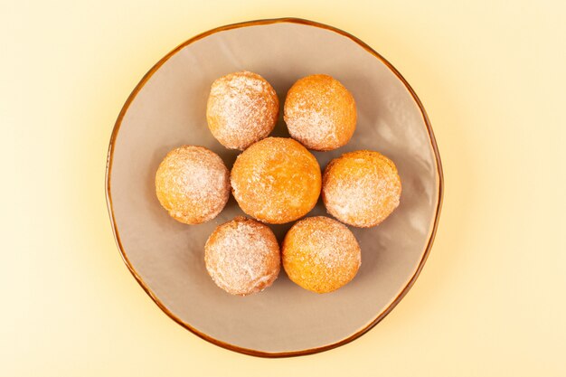 Une vue de dessus des gâteaux en poudre de sucre rond sucré cuit au four délicieux petits gâteaux à l'intérieur de la plate-forme ronde et fond crème boulangerie biscuit sucré