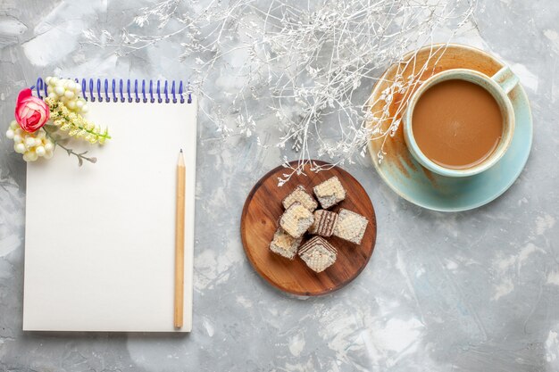 Vue de dessus des gaufres avec bloc-notes et café au lait sur le bureau gris-blanc biscuit au chocolat boire du café