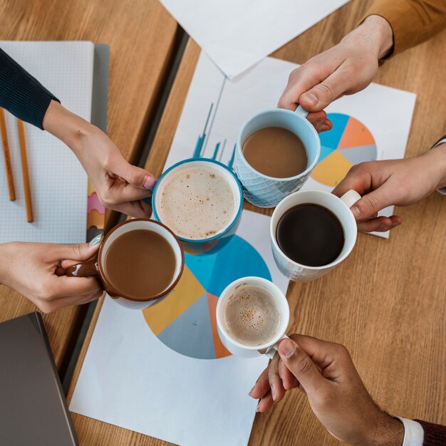 Vue de dessus des gens applaudissant avec des tasses à café pendant la réunion de bureau