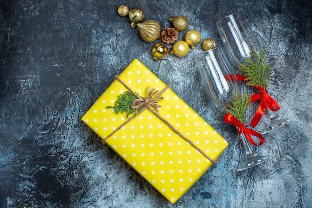 Photo gratuite vue de dessus des gobelets en verre avec ruban rouge et accessoires de décoration à côté d'une boîte-cadeau jaune sur une table sombre