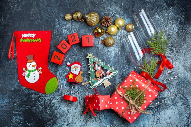 Vue de dessus des gobelets en verre tombés et des couverts, des accessoires de décoration, une boîte-cadeau et des numéros de chaussettes de Noël sur une table sombre