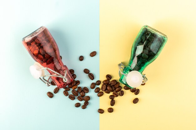 Une vue de dessus des graines de café brun à l'intérieur de bocaux en verre coloré sur la surface bleu-jaune boisson aux graines de café couleur photo
