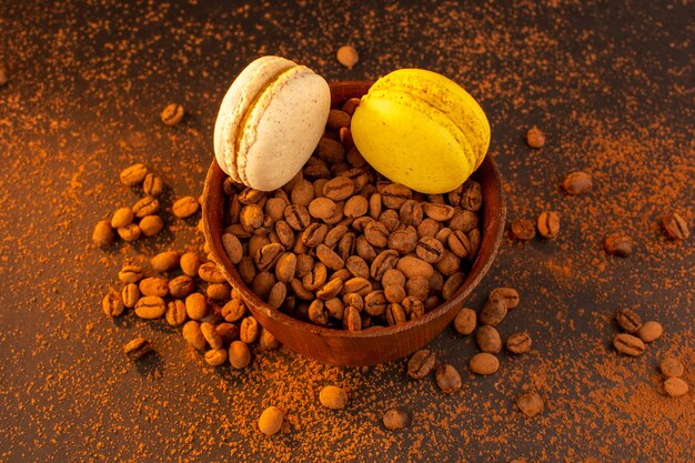 Une vue de dessus des graines de café brun à l'intérieur de la plaque brune avec des macarons sur la table marron