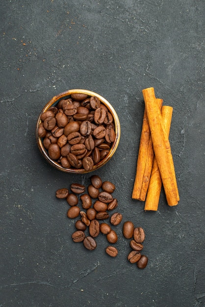 Vue de dessus des graines de café dans un bol de bâtons de cannelle sur fond sombre isolé