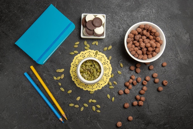 Vue de dessus des graines de citrouille fraîches avec des flocons de chocolat et des biscuits sur fond gris