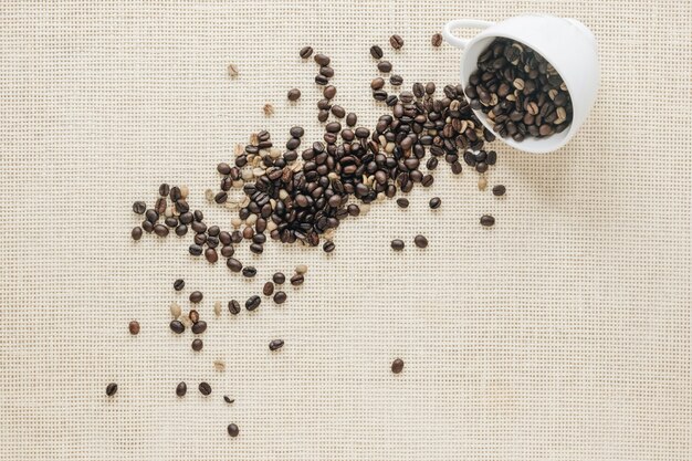 Vue de dessus des grains de café crus et torréfiés tombant d&#39;une tasse en céramique