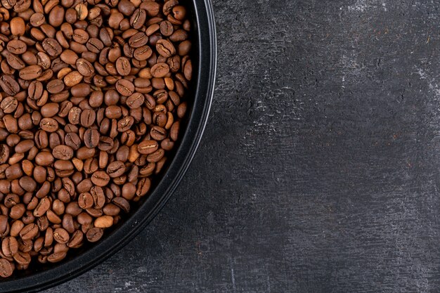 Vue de dessus des grains de café dans une casserole noire sur une surface sombre