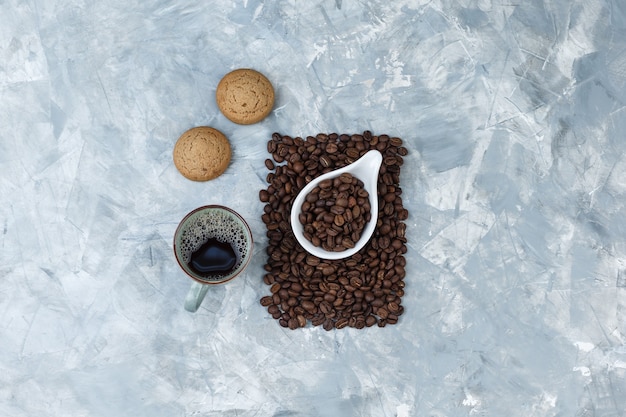 Vue de dessus des grains de café dans une cruche en porcelaine blanche avec des biscuits, une tasse de café sur fond de marbre bleu. horizontal