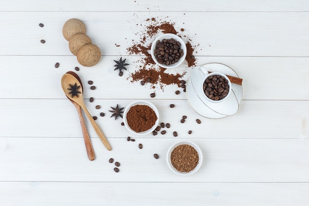 Vue de dessus des grains de café dans une tasse et un bol avec du café moulu, des épices, des biscuits, des cuillères en bois sur fond en bois. horizontal