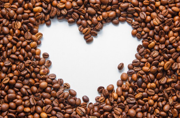 Vue de dessus des grains de café avec une forme de coeur vide sur fond blanc. horizontal