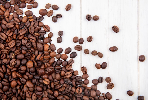 Vue de dessus des grains de café torréfiés foncés isolés sur un fond en bois blanc