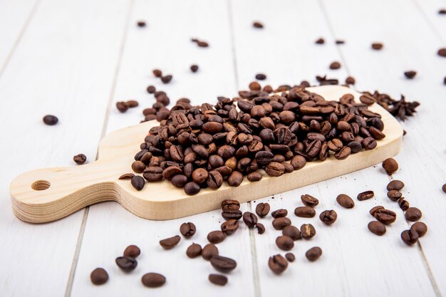Vue de dessus des grains de café torréfiés frais sur une planche de cuisine en bois sur un fond en bois blanc